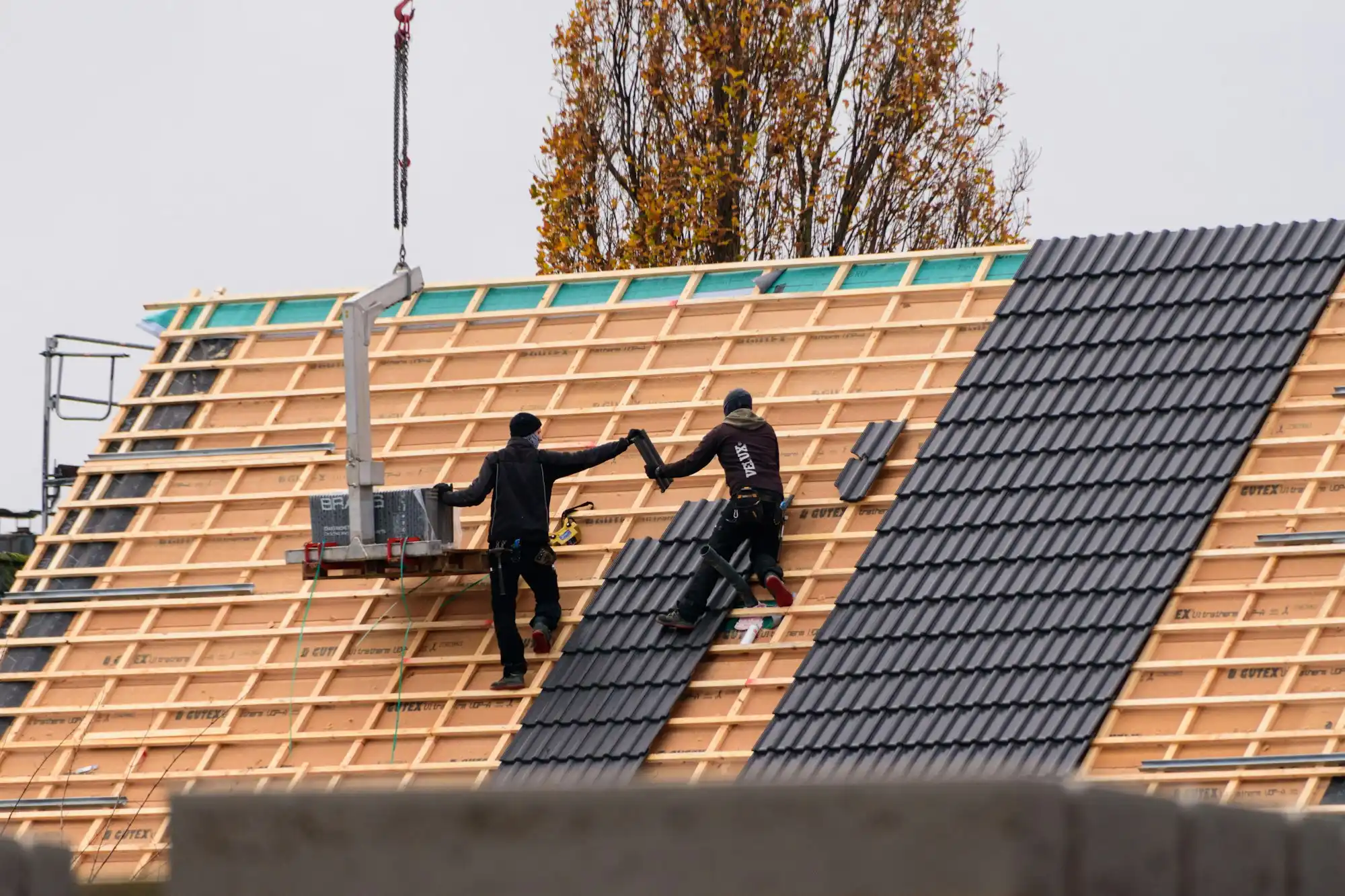 Neueindeckung eines Steildachs: neue Ziegel werden per Kran auf die Lattung gebracht